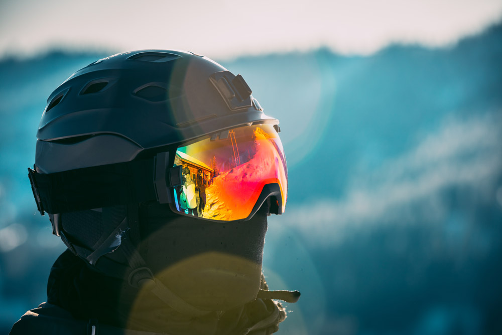 Skier wearing goggle and helmet atop mountain.